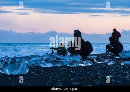 Fotografen mit schmelzenden Stücken aus klarem Gletschereis, die ursprünglich vom Breiðamerkurjökull-Gletscher in die Lagune von Jökulsárlón eingekalbt wurden, bei Diamond Beac Stockfoto