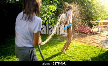 Zwei Teenager-Mädchen spielen Wasserkampf und Spritzwasser aus Gartenschlauch Stockfoto