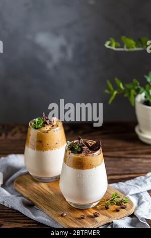 Zwei Gläser Iced Dalgona Coffee, ein trendiger, flauschiger, cremiger Schlagkaffee, dekoriert mit Thymian und dunkler Schokolade. Dunkler rustikaler Stil. Stockfoto