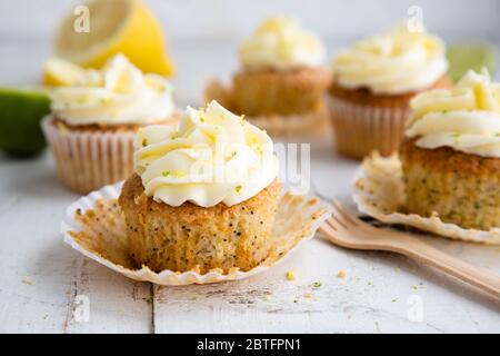 Cupcakes mit Zitronen- und Mohn-Samen mit Käsecreme-Zuckerguss und Zitronen- und Limettenschale auf einem rustikalen weißen Holztisch Stockfoto