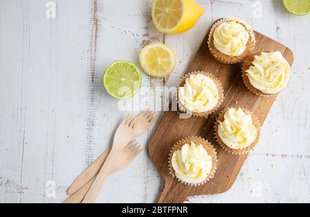 Cupcakes mit Zitronen- und Mohn-Samen mit Käsecreme-Zuckerguss und Zitronen- und Limettenschale auf einem rustikalen weißen Holztisch. Draufsicht Stockfoto