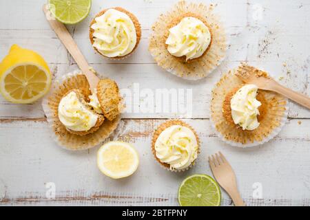 Cupcakes mit Zitronen- und Mohn-Samen mit Käsecreme-Zuckerguss und Zitronen- und Limettenschale auf einem rustikalen weißen Holztisch. Draufsicht Stockfoto