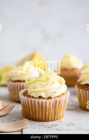 Cupcakes mit Zitronen- und Mohn-Samen mit Käsecreme-Zuckerguss und Zitronen- und Limettenschale auf einem rustikalen weißen Holztisch Stockfoto