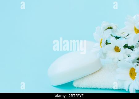 Auf einem weißen Handtuch ist ein Stück handgemachte Seife. Blumen von Gänseblümchen liegen in der Nähe. Stockfoto