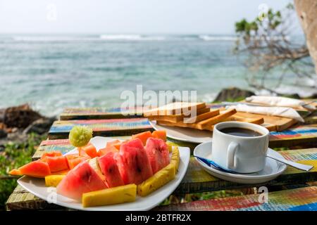 Leckeres Frühstück in der Nähe des Meeres. Meereswellen im Hintergrund. Romantischer Kurzurlaub im Paradies. Bunte Obstteller mit Ananas Stockfoto