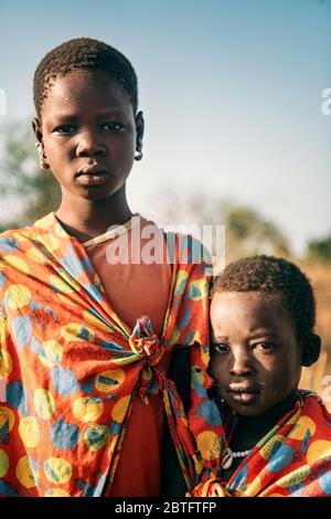 BOYA STAMM, SÜDSUDAN - 10. MÄRZ 2020: Kinder aus Boya Tribe tragen Stücke von hellen Stoffen und schauen auf Kamera, während sie auf verschwommen stehen Stockfoto