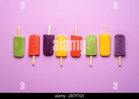 Eiscreme Popsicles Vielfalt auf einem lila Hintergrund aufgereiht. Flacher Lay von Multi-aromatisierten Eis auf Sticks. Erfrischendes veganes Dessert. Stockfoto