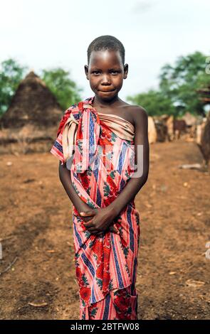 TOPOSA STAMM, SÜDSUDAN - 12. MÄRZ 2020: Mädchen in floralen Stoff umhüllt suchen und Kamera und lächelnd während der Leben in Toposa Tribe Dorf im Süden Stockfoto