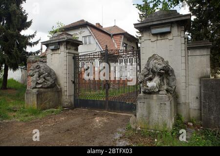 Verlassene Tor des Unteren Palastes (Dolní zámek) in Panenské Břežany in Mittelböhmen, Tschechische Republik. Das Schloss gehörte dem jüdischen Zuckerproduzenten Ferdinand Bloch-Bauer und seiner Frau Adele Bloch-Bauer, die als Vorbild für das berühmte Porträt des österreichischen Malers Gustav Klimt bekannt war. Während der Nazi-Besetzung diente der Palast als Residenz für Reinhard Heydrich, der stellvertretender Beschützer von Böhmen und Mähren war. Am 27. Mai 1942 ging er durch dieses Tor zu Beginn seiner berüchtigten Reise nach Prag, wo er von tschechoslowakischen Soldaten als Folge der Operation Anthropoid schwer verletzt wurde. Stockfoto