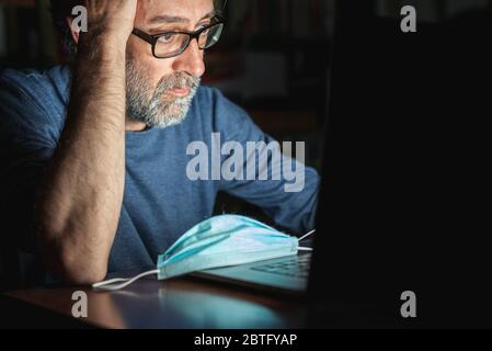 Reifer Mann, der auf dem Computer die Nachrichten über die globale Pandemie von Corona-Virus und er Sorgen, emotionale Not, Schlaflosigkeit, Sorge für Unternehmen Stockfoto