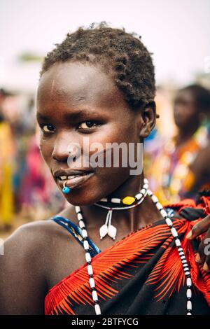 TOPOSA TRIBE, SÜDSUDAN - 12. MÄRZ 2020: Junge Frau mit stechenden und kurzen Haaren lächelnd und mit Blick auf die Kamera während sie in Toposa Tribe lebt Stockfoto