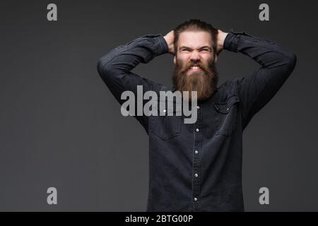 Bärtiger Mann in Wut schreit laut mit Mund auf grauem Hintergrund geöffnet. Stockfoto