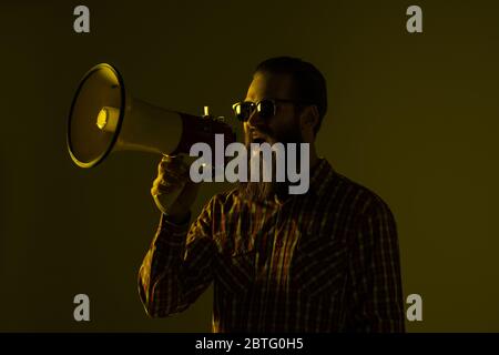 Fashion Portrait des emotionalen Hipster-Mannes mit Megaphon auf weißem Hintergrund in stilvoller Sonnenbrille. Verkäufer mit Megaphon schreien Stockfoto