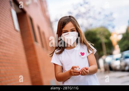 Kleines Mädchen trägt Maske desinfizierend ihre Hände mit Hydroalkoholgel. Stockfoto