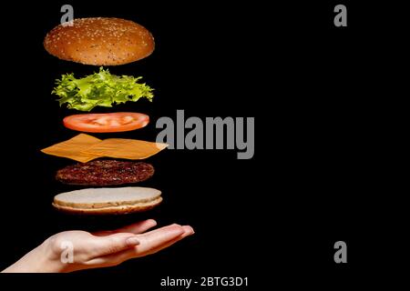 Fliegende Zutaten Burger oder Cheeseburger auf einem kleinen Holzschnittbrett isoliert auf dunklem Hintergrund. Burger schwimmt in der Luft über dem Tisch Stockfoto