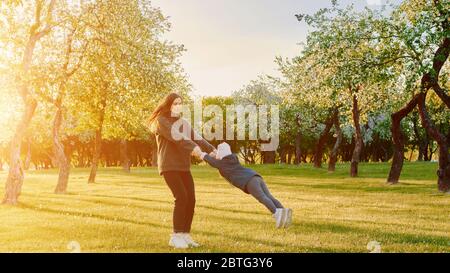 Mutter mit Kindern, die bei Sonnenuntergang in einem Park spielen. Frau wirbelt Tochter. Aktives übergeordnetes Element mit untergeordneten Elemente Stockfoto