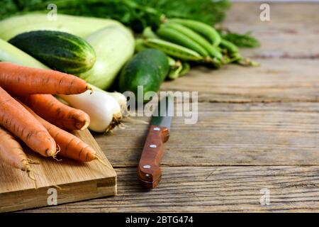 Verschiedene frische Gemüse. Erbsen, Karotten, Gurken, Zucchini, Zwiebel und Küchenmesser auf einem Holztisch mit Kopierfläche für Text. Selektiver Fokus. Stockfoto
