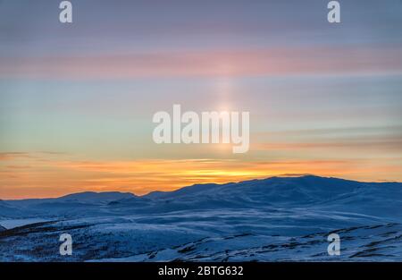 Sehr schöner Sonnenuntergang in den skandinavischen Bergen - rote orangefarbene Sonnenstrahlen, die den weißen Schnee und den blauen Himmel färben, die Sonne scheint wie ein Laserstrahl Stockfoto