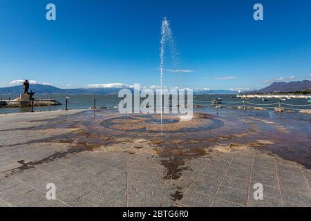 Brunnen, der den Boden mit einem Wasserstrahl auf der Promenade des Sees Chapala, der Pier und die Berge im Hintergrund, sonnigen Tag mit einem Klea Stockfoto