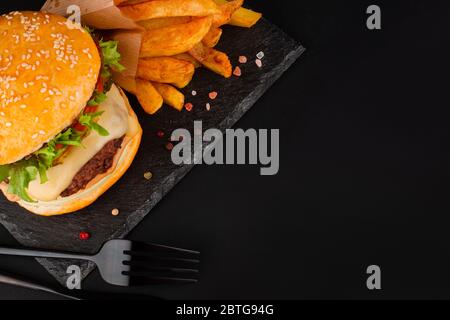 Ein großer klassischer Hamburger mit pommes frites auf schwarzem Steinteller auf schwarzem Hintergrund und Platz für Text Stockfoto