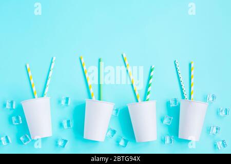 Weiße Papierkappen mit farbigem Cocktail Stroh und Eis auf blauem Hintergrund. Raum für Text. Recycling Öko Konzept. Pop Art Stil. Party Stockfoto