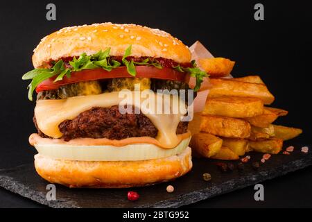 Ein großer klassischer Hamburger mit pommes frites auf schwarzem Steinteller auf schwarzem Hintergrund und Platz für Text Stockfoto