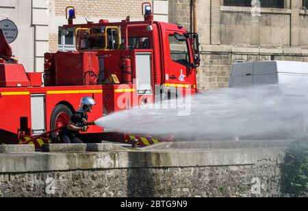 Französische Feuerwehrleute Training Bohrer mit einem Feuerwehrschlauch, um Hochdruckwasser vor einem roten Feuerwehrauto entlang des Canal de l'Ourcq geparkt sprühen. Stockfoto