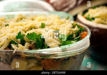 Kartoffeln in Töpfen zum Backen vorbereiten. Rohe Kartoffeln, Fleisch, Zwiebeln, Karotten, Petersilie, Käse im Glas und Keramikbecher aus nächster Nähe. Bereit zum Backen. Stockfoto