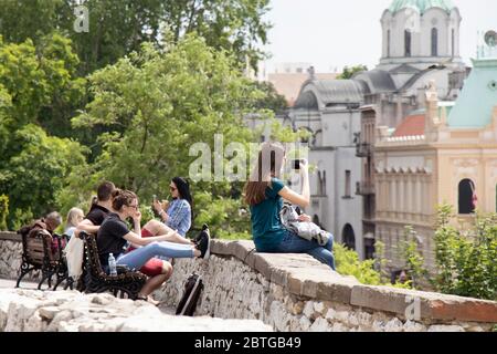 Belgrad, Serbien - 21. Mai 2020: Mädchen im Teenageralter, das auf einer Mauer der Festung Kalemegdan sitzt und mit dem Handy den Blick auf die Stadt filmt, und eine Gruppe junger Menschen Stockfoto