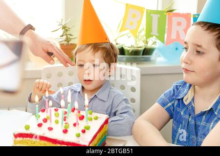 Kinder Geburtstagsfeier. Kind bläst Kerzen auf bunten Kuchen aus Stockfoto