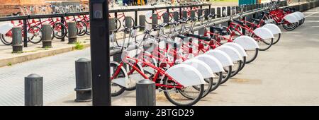 Viele rote Fahrräder - City-Fahrräder sind ordentlich aufgereiht und bereit zum Mieten. Bild mit Details und ist hauptsächlich rot gefärbt. Stockfoto