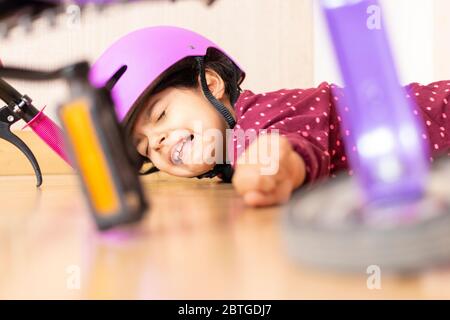 Trauriges kleines Mädchen fiel auf den Boden, während sie mit ihrem Fahrrad im Haus spielte Stockfoto