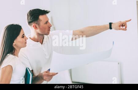 Designerin und ein junger Mann stehen in einer leeren Wohnung. Stockfoto