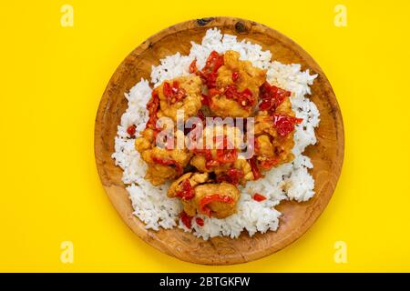 Reis mit Hühnernuggets, bestreut mit Chilisauce, wird in einem Holzteller auf gelbem Hintergrund serviert. Stockfoto