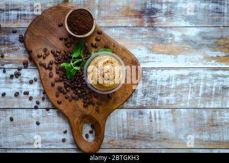 Dalgona Kaffee wird auf einem Schneidebrett mit Kaffeebohne Ornamenten serviert und von oben fotografiert. Stockfoto