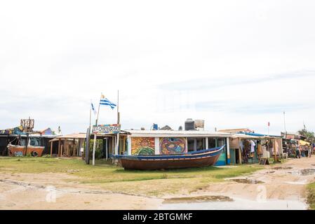 Cabo Polonio, Rocha / Uruguay; 30. Dez 2018: Boot und Einkaufsstraße in der Stadt, Handwerk und Kleidung Geschäfte. Eine uruguayische Flagge flattert im Wind. Stockfoto