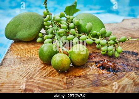 Frische grüne unreife Trauben, Mandarinen und Mangos auf einem Holzhintergrund in blauem Wasser und Kopierraum. Stockfoto