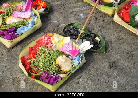 Opfergaben Set balinesischer und indonesischer Ritus Angebot an Gottheitsengel gott des Wassers im Meer auf Bodensand am Kuta Beach in Bali, Indonesien Stockfoto