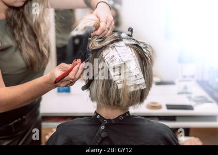 Master Friseur im Schönheitssalon Färbung Haar der jungen Frau mit Aluminiumfolie. Selektiver Fokus Stockfoto