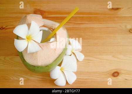 Natürlicher junger Kokosnusssaft und Fruchtfleisch in der Schale mit Plumeria Blüten auf einem Holztisch Stockfoto