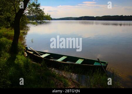 Ein kleines Holzboot am Ufer eines Sees während eines ruhigen, klaren Sommertages mit nahem Sonnenuntergang. Im Nationalpark Aukštaitija in Litauen. Stockfoto