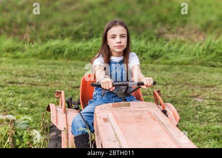 Junges Mädchen auf einem Traktor in einem grünen Feld. Stockfoto