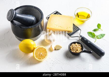 Grünes Basilikum Pesto alla Genovese italienische Rezepturzutaten auf weißer Tafel von der Seitenansicht. Parmesan, Basilikumblätter, Pinienkerne, Olivenöl, ga Stockfoto