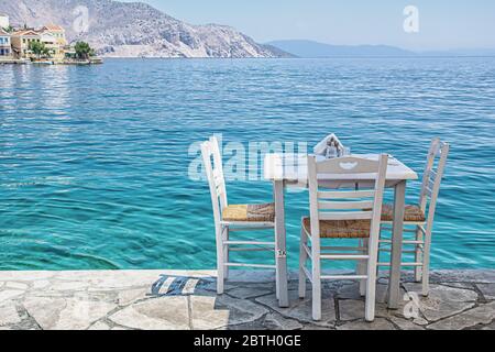 Weiße Stühle mit Tischen in typisch griechischer Taverne am Meer in Symi Stadt Stockfoto