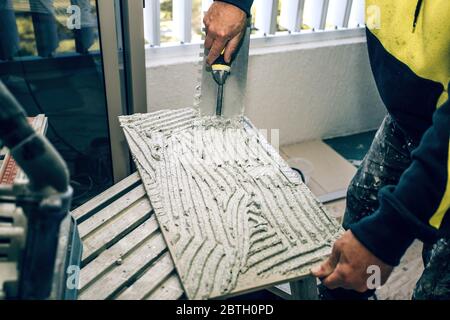 Professioneller Baumeister verschmiert Zementleim auf der Keramikfliesen mit einer Kelle. Konzept Renovierung Reparatur, Überholung, Auftragskachel. Stockfoto