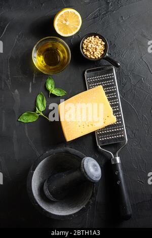 Zutaten für grünes Pesto auf schwarzem Stein Hintergrund Parmesan Käse, Basilikumblätter, Pinienkerne, Olivenöl, Knoblauch Mörser Draufsicht. Stockfoto