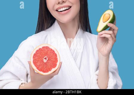 Lächelnde junge Frau mit einer Hälfte Avocado und einer Scheibe Grapefruit Stockfoto