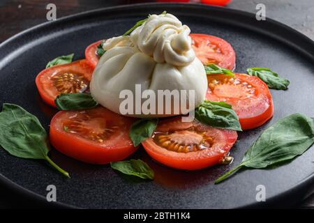 Handgemachter Burrata-Käse mit frischen Tomaten und Basilikumblättern serviert traditionellen italienischen Salat aus nächster Nähe. Stockfoto