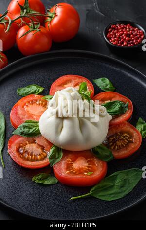 Büffelkäse mit frischen Tomaten und Basilikumblättern serviert. Auf schwarzem Stein Hintergrund Stockfoto