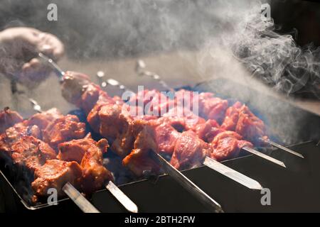 Mann Kochen marinierten Schaschlik, Lammfleisch Grillen auf Metall Spieß. Weißer Rauch. Verkauf. Nahaufnahme. Unschärfe Stockfoto